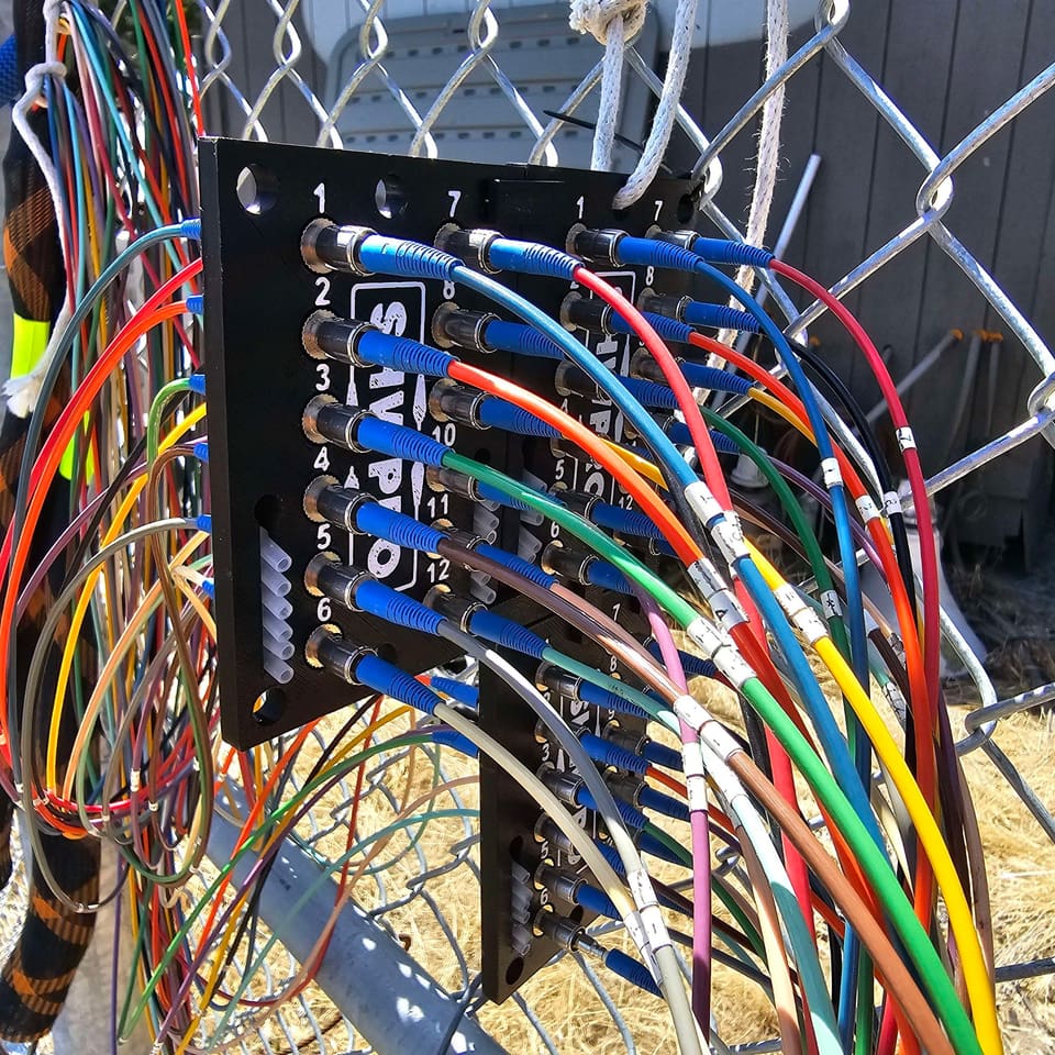 ST Patch Panel zip tied to a chain link fence with blue and colored fiber jumpers patched in
